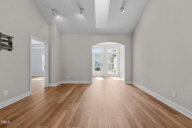 spare room with arched walkways, vaulted ceiling, wood finished floors, and baseboards