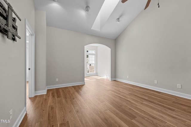 empty room with ceiling fan, arched walkways, wood finished floors, and baseboards