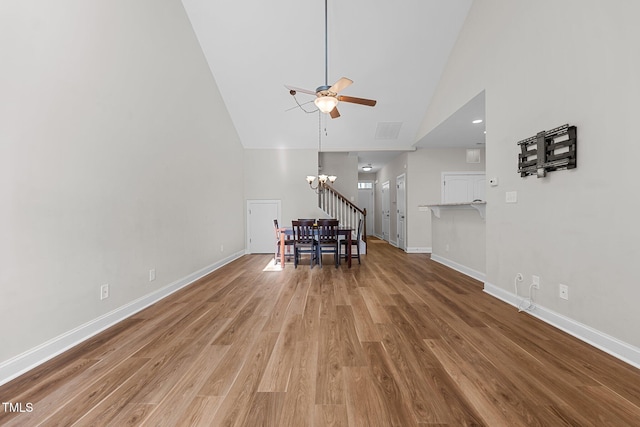 living room featuring high vaulted ceiling, baseboards, wood finished floors, and ceiling fan with notable chandelier