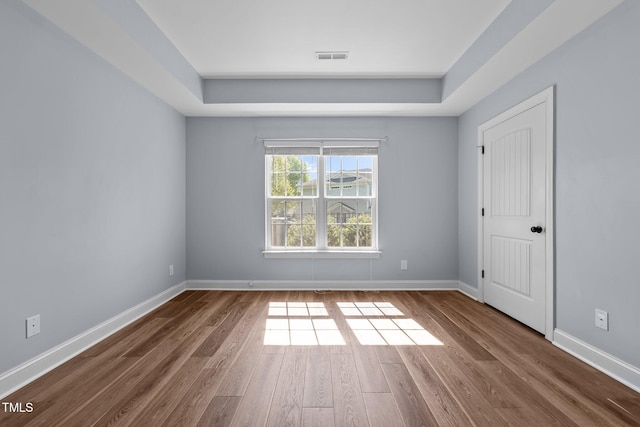 empty room featuring visible vents, baseboards, wood finished floors, and a tray ceiling