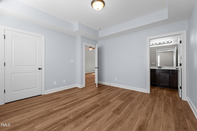 unfurnished bedroom featuring a tray ceiling, light wood-type flooring, and baseboards