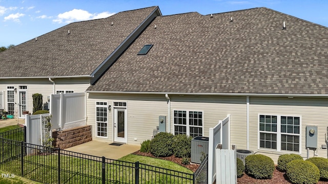 back of property featuring a fenced backyard, a shingled roof, central air condition unit, a patio area, and a lawn