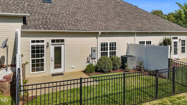rear view of house featuring a lawn, roof with shingles, central AC, and fence private yard