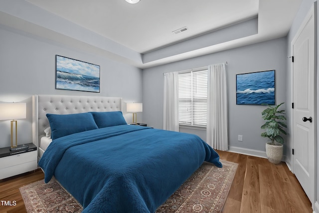 bedroom with baseboards, wood finished floors, visible vents, and a tray ceiling