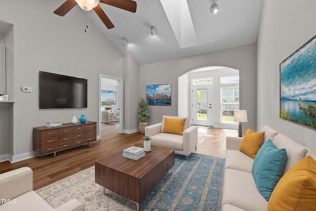living room with arched walkways, baseboards, a ceiling fan, wood finished floors, and high vaulted ceiling