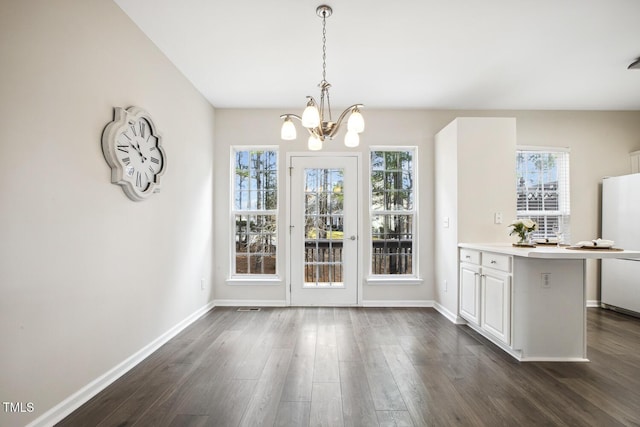 unfurnished dining area featuring a notable chandelier, dark wood-style flooring, and baseboards