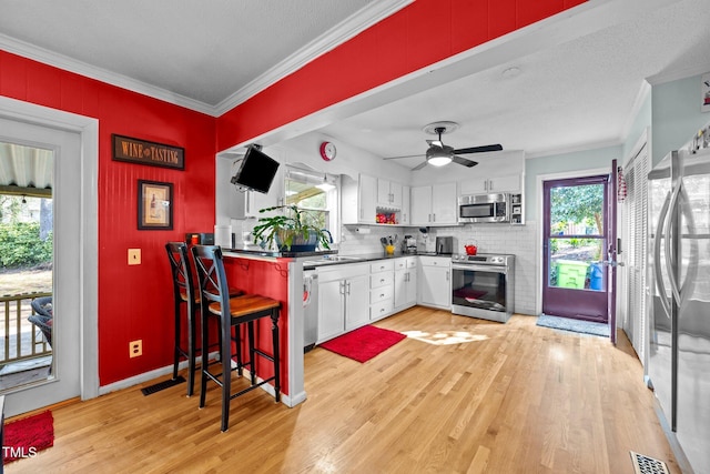 kitchen with white cabinetry, light wood-style floors, ornamental molding, appliances with stainless steel finishes, and dark countertops