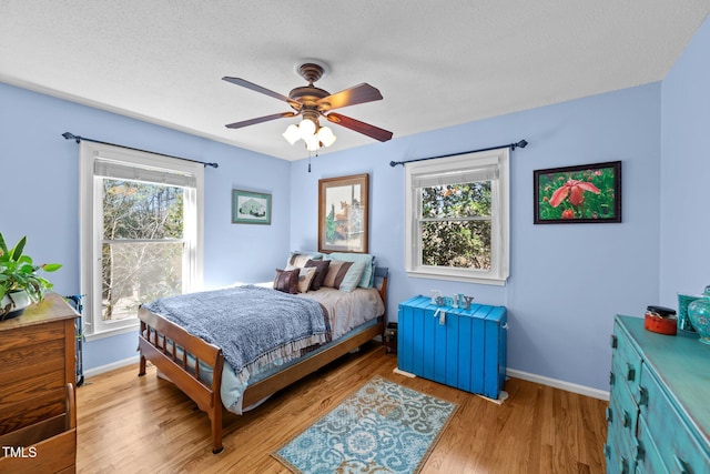 bedroom featuring baseboards, multiple windows, a textured ceiling, and light wood-style floors