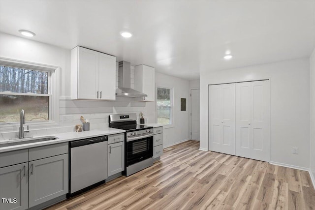 kitchen featuring appliances with stainless steel finishes, wall chimney range hood, light hardwood / wood-style floors, sink, and white cabinetry