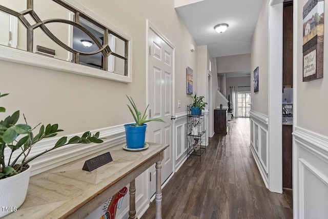 corridor with wainscoting, dark wood finished floors, and a decorative wall