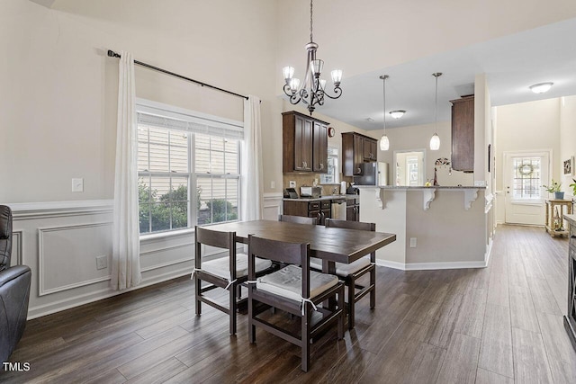 dining room with dark wood-type flooring, a decorative wall, wainscoting, and an inviting chandelier