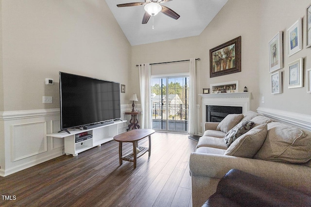 living area featuring ceiling fan, a decorative wall, a wainscoted wall, a fireplace, and dark wood-style floors