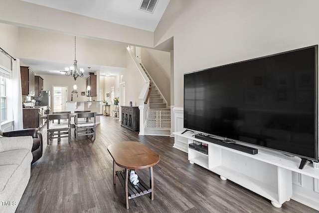 living area featuring dark wood-style flooring, a notable chandelier, lofted ceiling, visible vents, and stairway