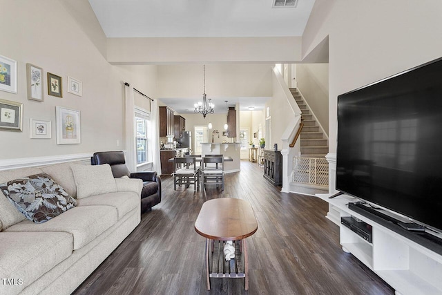 living room featuring a notable chandelier, visible vents, a towering ceiling, dark wood-type flooring, and stairs