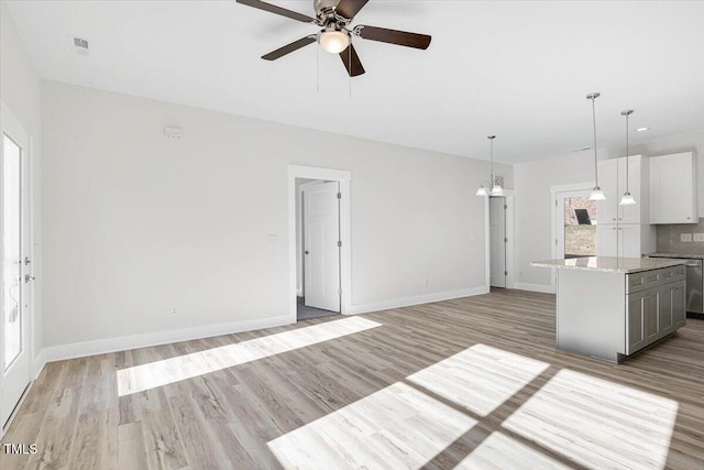 kitchen with gray cabinets, light hardwood / wood-style flooring, hanging light fixtures, light stone counters, and a kitchen island