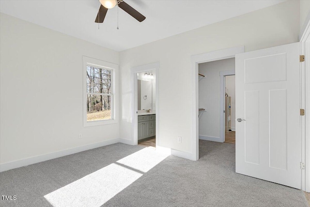 unfurnished bedroom with water heater, ceiling fan, ensuite bathroom, a spacious closet, and light colored carpet