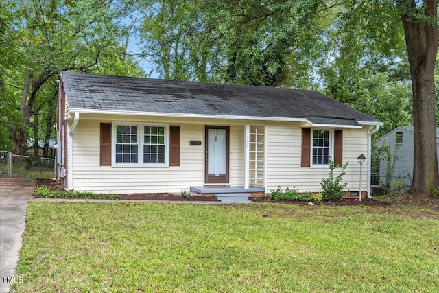 ranch-style home featuring a shingled roof, a front yard, and fence