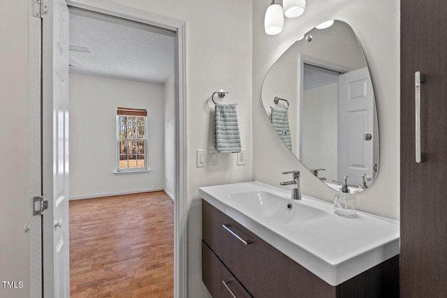 bathroom with baseboards, vanity, a textured ceiling, and wood finished floors