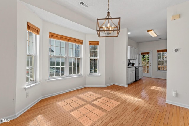 unfurnished dining area with baseboards, visible vents, light wood finished floors, and an inviting chandelier