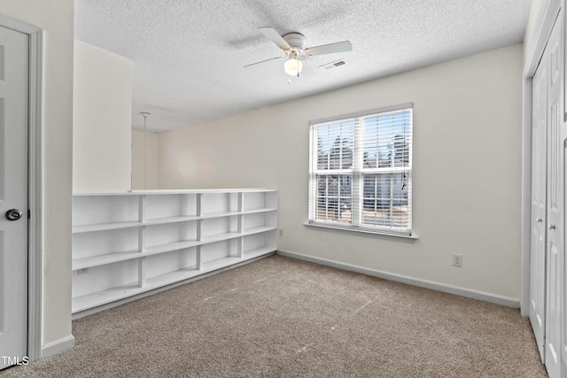 carpeted empty room with a ceiling fan, visible vents, a textured ceiling, and baseboards