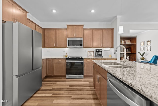 kitchen with hanging light fixtures, stainless steel appliances, light hardwood / wood-style floors, sink, and ornamental molding