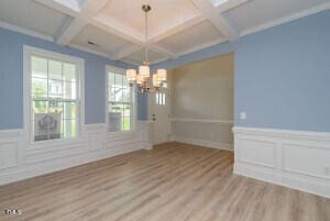 unfurnished dining area featuring beamed ceiling, coffered ceiling, a chandelier, and light hardwood / wood-style flooring