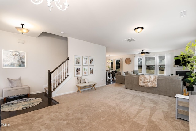 carpeted living room with a fireplace, visible vents, stairway, a ceiling fan, and baseboards