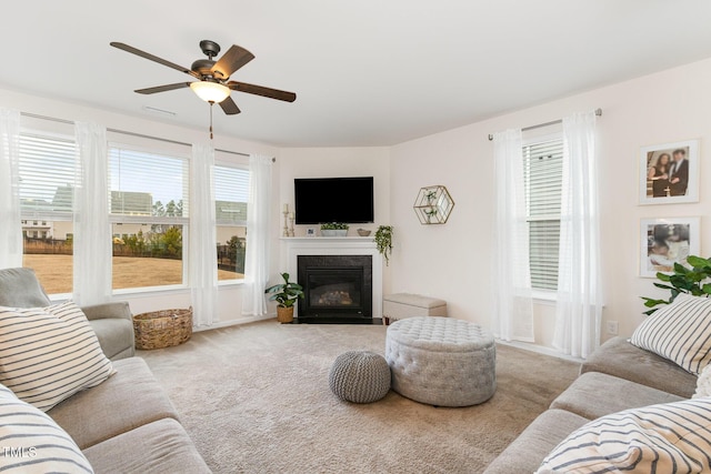 living area with carpet, a ceiling fan, and a fireplace with flush hearth