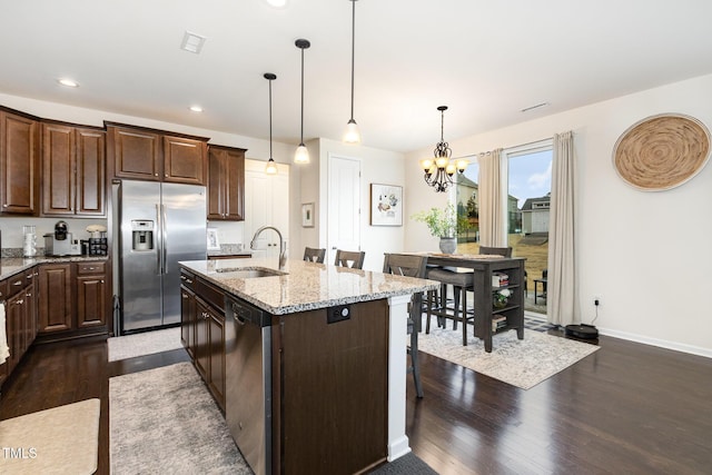 kitchen with light stone counters, appliances with stainless steel finishes, a sink, and dark wood finished floors