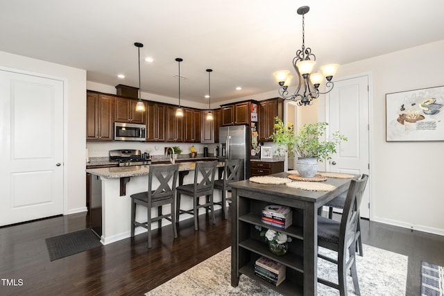 kitchen featuring a breakfast bar, a center island, appliances with stainless steel finishes, light stone countertops, and dark wood finished floors