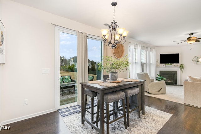 dining space with a fireplace with flush hearth, ceiling fan with notable chandelier, baseboards, and wood finished floors