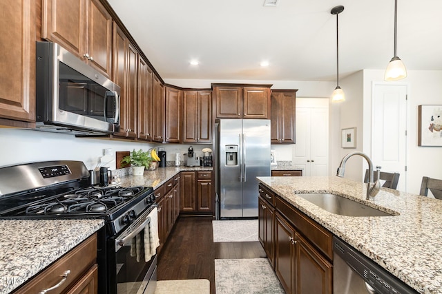 kitchen featuring light stone counters, dark wood-style floors, hanging light fixtures, appliances with stainless steel finishes, and a sink