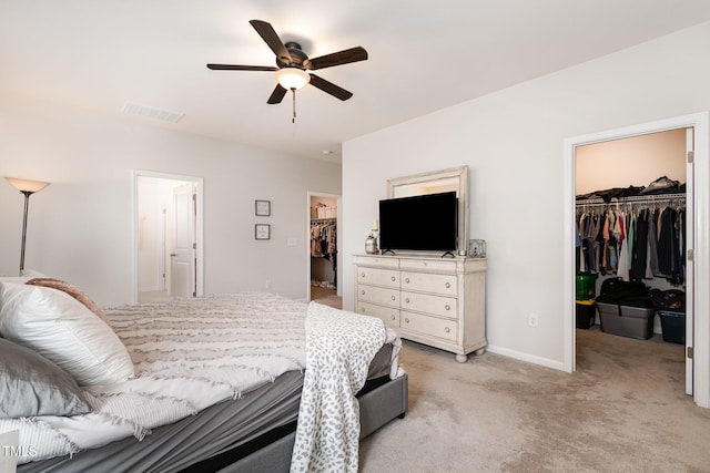 bedroom featuring light colored carpet, visible vents, baseboards, a closet, and a walk in closet