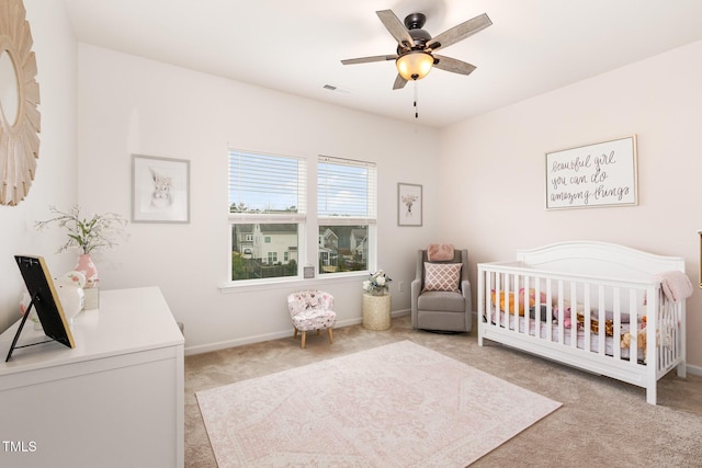 bedroom with a ceiling fan, visible vents, baseboards, a crib, and carpet