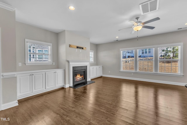 unfurnished living room with a wealth of natural light, a glass covered fireplace, visible vents, and wood finished floors