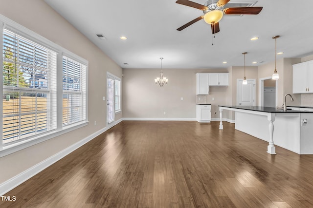 unfurnished living room with recessed lighting, ceiling fan with notable chandelier, dark wood-style flooring, visible vents, and baseboards