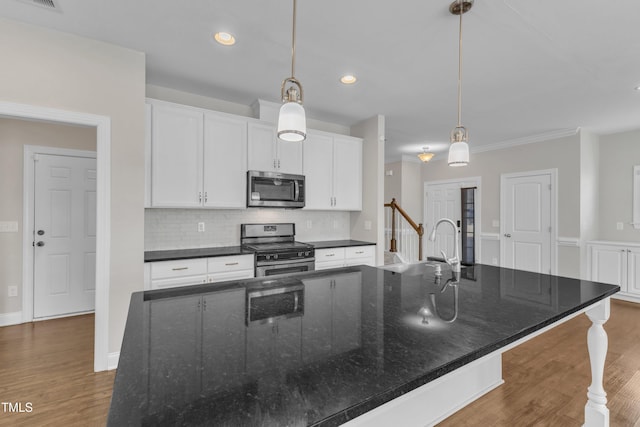 kitchen featuring stainless steel appliances, backsplash, white cabinets, wood finished floors, and a large island with sink