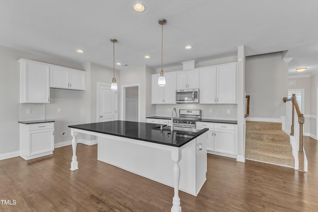 kitchen with appliances with stainless steel finishes, dark countertops, a sink, and dark wood-style floors