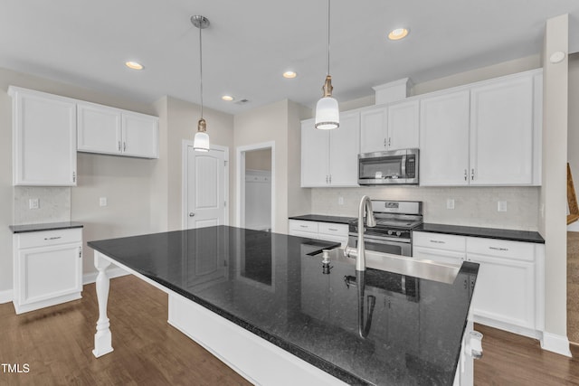 kitchen featuring dark wood-style floors, stainless steel appliances, a center island with sink, and white cabinetry