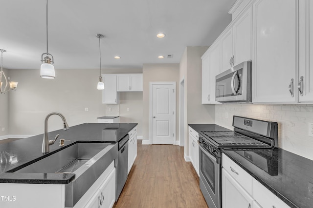 kitchen with wood finished floors, a sink, white cabinetry, appliances with stainless steel finishes, and tasteful backsplash