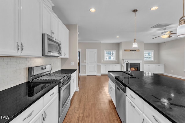 kitchen featuring a warm lit fireplace, tasteful backsplash, stainless steel appliances, white cabinetry, and a sink