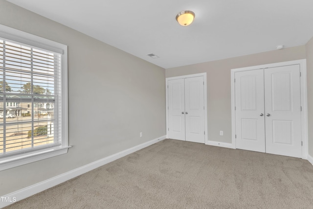 unfurnished bedroom with visible vents, baseboards, two closets, and carpet flooring