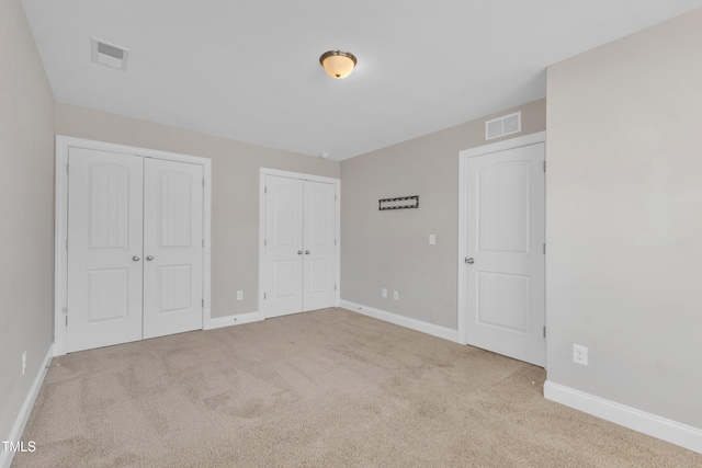 unfurnished bedroom featuring carpet floors, baseboards, visible vents, and two closets