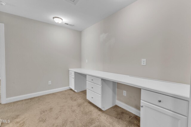 unfurnished office featuring light carpet, baseboards, visible vents, and built in study area