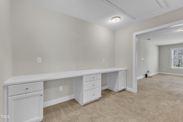 unfurnished office with light colored carpet, built in desk, and baseboards