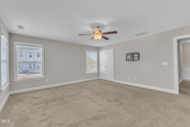 carpeted spare room with a ceiling fan, visible vents, and baseboards