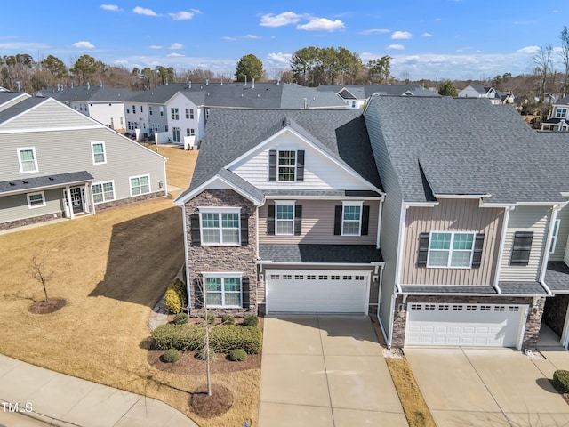 traditional-style house featuring a shingled roof, an attached garage, a residential view, stone siding, and driveway