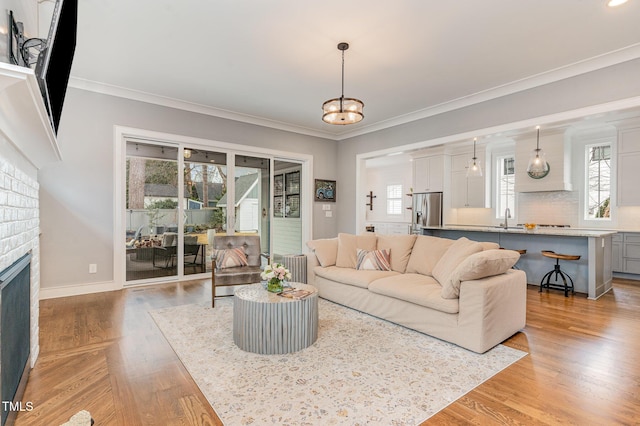 living room featuring ornamental molding, a brick fireplace, sink, and light hardwood / wood-style flooring