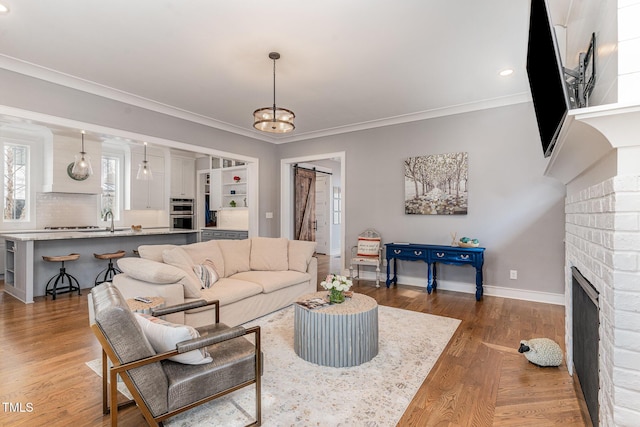 living room featuring hardwood / wood-style floors, a fireplace, sink, crown molding, and a barn door