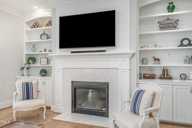 living area featuring built in shelves, light wood-type flooring, a fireplace, and ornamental molding